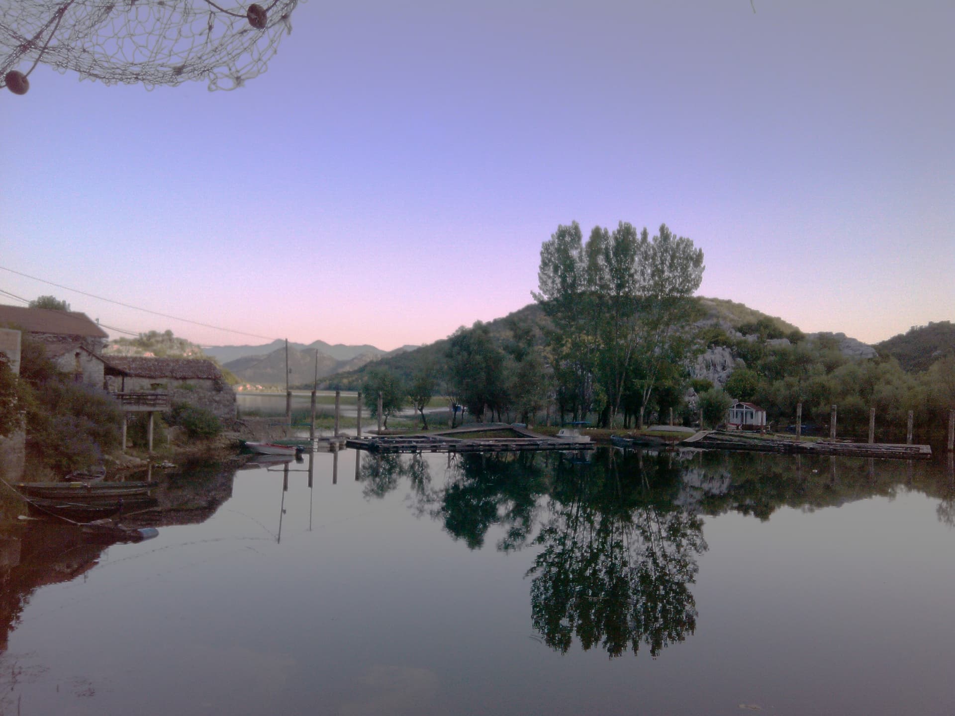Calm Karuč bay at dusk with stone fishing houses, wooden docks and nets over still water